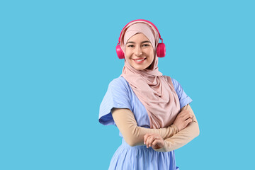 Beautiful young Muslim woman in hijab and modern headphones on blue background