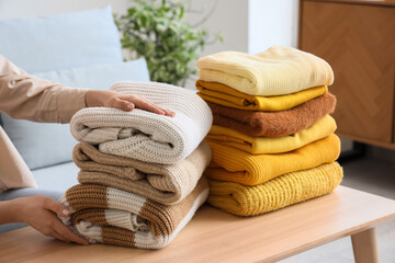 Woman putting stacks of warm clothes on wooden table at home