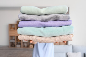 Woman holding stack of different clean clothes at home