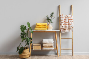 Table with clean clothes, eucalyptus branches, beautiful houseplant and ladder near light wall