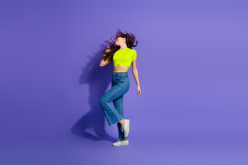 Energetic young woman in a vibrant outfit enjoying motion against a violet background, radiating positivity