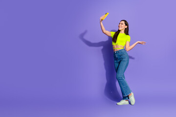 Stylish woman on purple background posing confidently while taking a selfie, expressing joy, casual...