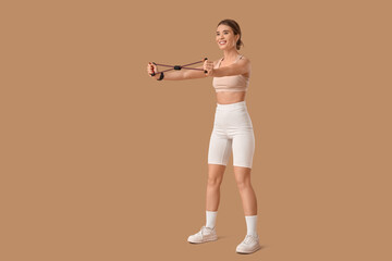 Sporty young woman exercising with fitness expander on beige background