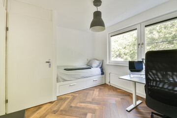 A contemporary bedroom featuring a bed with grey bedding, a desk with a computer, and large windows allowing natural light to brighten the space.