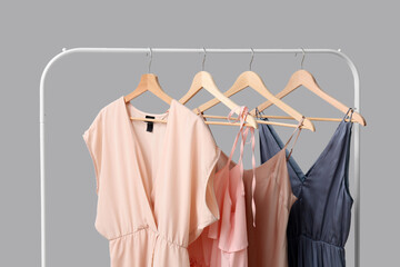 Beautiful female dresses hanging on rack against grey background