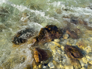 dynamic river stream with sunlit stones and flowing crystal clear water. balanced composition with contrast between dark rocks and bright