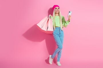 Stylish young woman with shopping bags posing against a pink background, exemplifying fashion