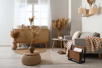 Interior of stylish living room with grey sofa, wooden cabinet and pampas grass