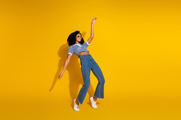 Stylish young woman in casual denim with striped top, posing energetically against a vibrant yellow background