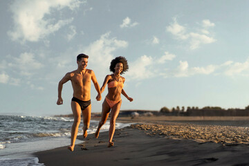 Happy interracial couple running hand in hand on the beach at sunset. Concept of freedom, love, a romantic summer vacation and a healthy, active lifestyle.