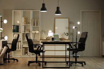 Interior of office with workplace, shelf unit and glowing lamps at night