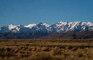 Idyllic calm serene Southern Alps snow capped mountain peaks winter panorama, grass landscape at Lake Emma, Ashburton Lakes, South Island, New Zealand