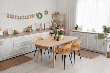 Interior of festive kitchen with tulip flowers, rabbits and Easter painted eggs on tree branches at dining table