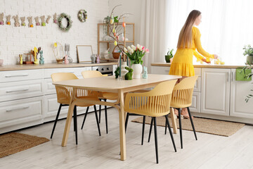 Woman with tulip flowers, rabbits and Easter painted eggs on tree branches in kitchen
