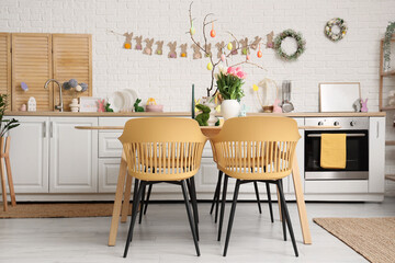 Interior of festive kitchen with tulip flowers, rabbits and Easter painted eggs on tree branches at dining table