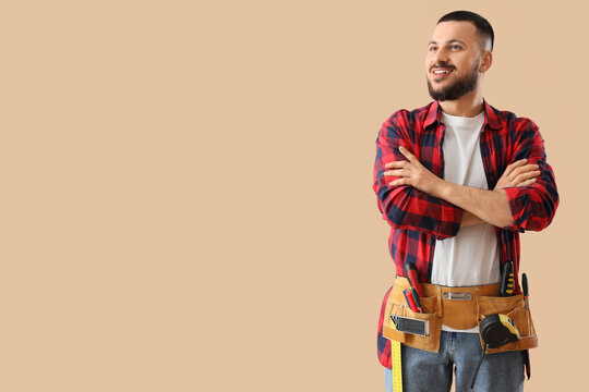 Happy male construction worker with professional tools on beige background