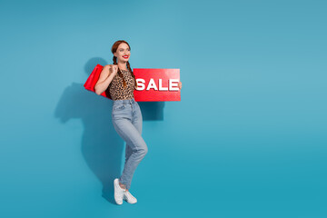 Young stylish woman holding sale sign while shopping, posing with a trendy leopard print top and...