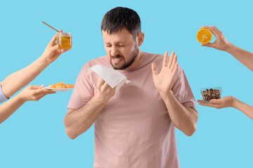 Sneezing young man and female hands with different products on blue background. Food Allergy...