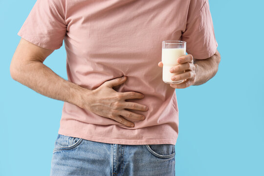 Young man with bellyache and glass of milk on blue background, closeup. Food Allergy Awareness Month