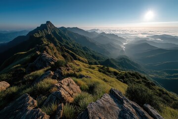 Panoramic mountain view from summit with sunlit green ridges and dramatic rocky shadows.