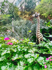 A whimsical garden scene features a decorative giraffe among vibrant green foliage and colorful flowers, creating a vibrant, playful atmosphere.