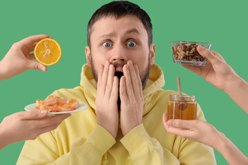 Shocked young man and female hands with products on green background, closeup. Food Allergy...