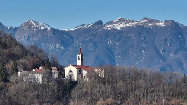Cinematic telephoto drone shot orbiting counterclockwise around the Church of Bolca, a quaint village in Verona&rsquo;s hills, with Monte Carega rising in the background.