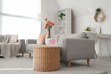 Obraz premium Vase with carnation flowers and card for Mother's Day on basket in living room interior