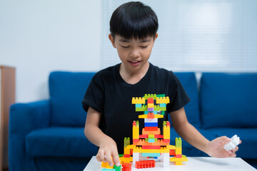 Asian boy is playing and building a robot with colorful plastic construction bricks at home, developing his creativity and problem-solving skills