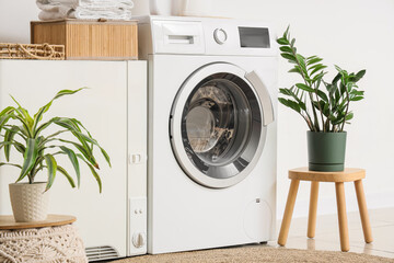 Interior of laundry room with modern washing machine and clothes dryer near white wall