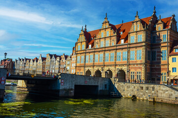 Scenic view of historic architecture and a bridge over a calm river in Gdansk, Poland. Bright day showcases ancient buildings reflecting in the water, offering cultural and travel allure.
