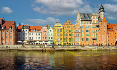 Fototapeta premium Charming historic architecture lines the waterfront of Gdansk under a clear blue sky. The river is bustling with boats, offering a vibrant scene with the city's iconic brick buildings
