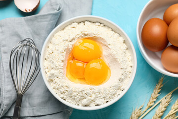 Bowl of flour, fresh chicken eggs, whisk and napkin on color background