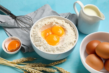 Bowl of flour with fresh chicken eggs, jug of milk and whisk on color background