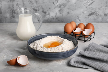 Bowl with flour with fresh chicken eggs and jug of milk on grunge table