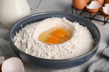 Bowl of flour with fresh chicken eggs on grunge table, closeup