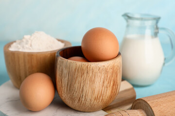 Bowls with fresh chicken eggs, flour and jug of milk on color background, closeup