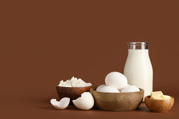 Wooden bowls with fresh chicken eggs, butter, flour and bottle of milk on color background