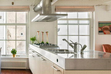 A sleek and contemporary kitchen featuring a metallic island, stylish decor, and ample natural...