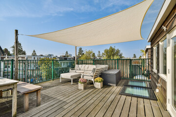 A stylish rooftop patio features comfortable seating, planters, and a protective shade sail,...
