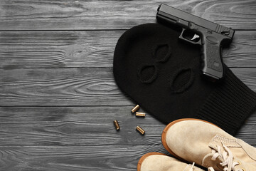 Balaclava with shoes, gun and bullets on grey wooden background with space for text