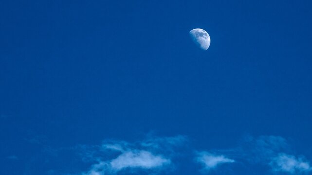 A waxing gibbous moon shines in a deep blue sky with wispy white clouds at the bottom. Tranquil night or twilight scene. - Powered by Adobe