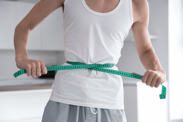 Young man with anorexia measuring his waist in kitchen, closeup
