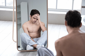 Young man with anorexia looking in mirror at home