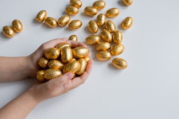 Childs hands holding golden chocolate Easter eggs on white background