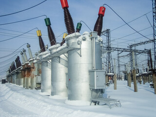 Obraz premium Power station equipment in winter covered by snow. Industrial electricity generation facility, electric power transmission and distribution system for engineering solution. Oil switch.