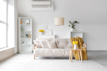 Interior of light living room with sofa, shelf units and daffodils in vases