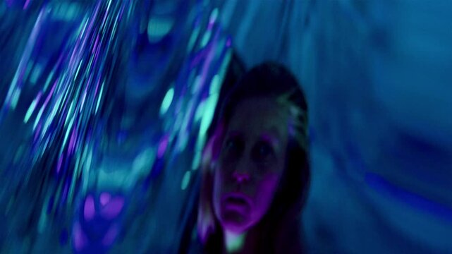 Beautiful female dancer performing graceful fluid movements in multicolored neon light, in front of distorting mirror creating surreal dreamlike reflections