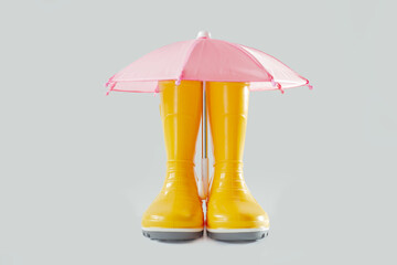Yellow rubber boots and pink umbrella on light grey background.