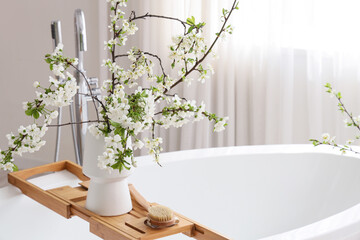 Vase with blossoming branches on bathtub in room